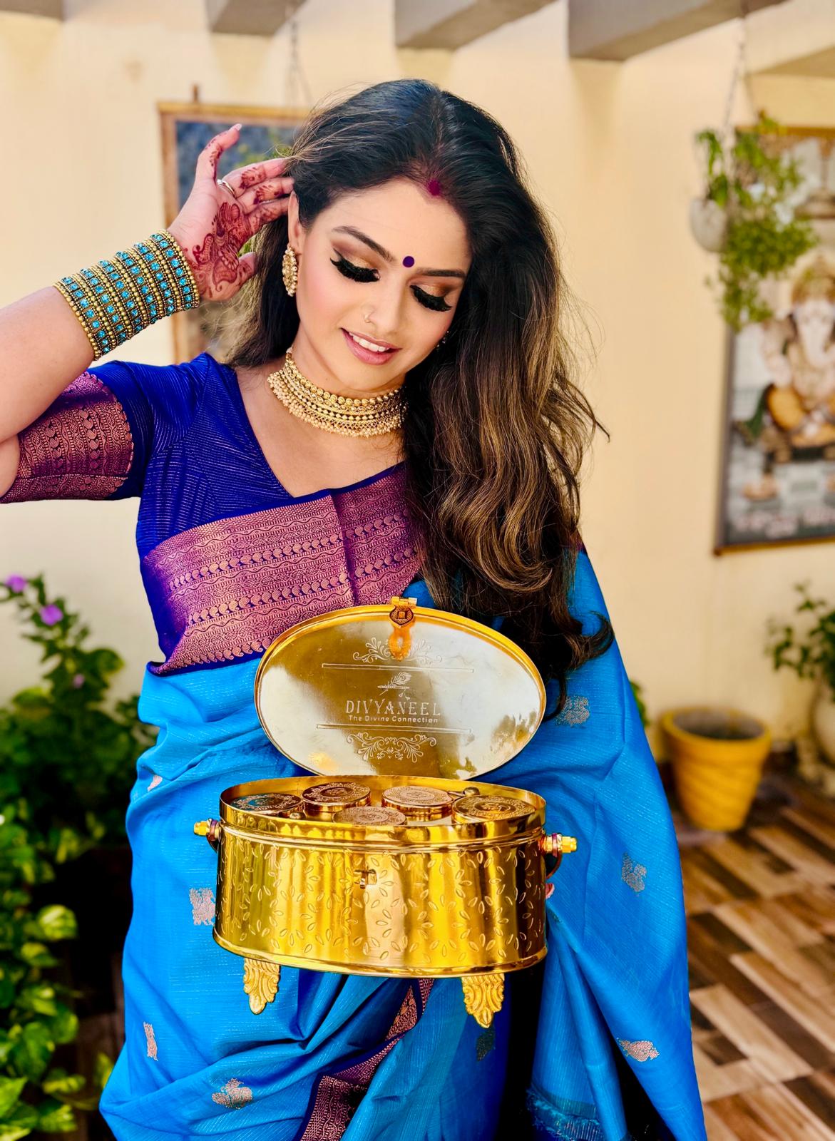 Woman in traditional attire holding a decorative metal item indoors.